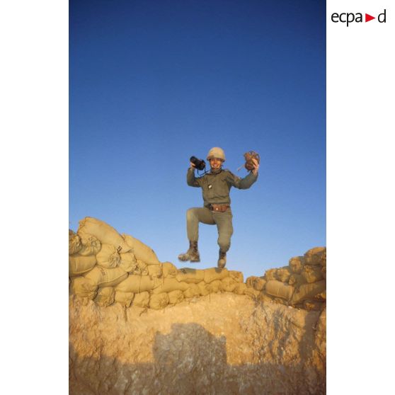 En ZDO (zone de déploiement opérationnel) Olive, un sergent-chef photographe de l'ECPA (Etablissement cinématographique et photographique des Armées), saute par-dessus le muret de sacs de sable dans son trou de combat.