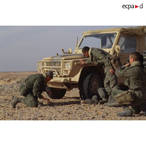 En ZDO (zone de déploiement opérationnel) Olive, le capitaine chef d'équipe, un adjudant preneur de son et un brigadier caméraman de l'équipe de l'ECPA (Etablissement cinématographique et photographique des Armées) autour de leur véhicule Peugeot P4 en dépannage par un quatrième homme.