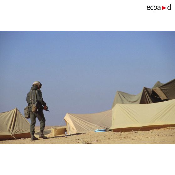 En ZDO (zone de déploiement opérationnel) Olive, un soldat armé d'un fusil d'assaut FAMAS déambule dans un campement.