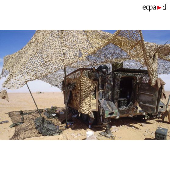 En ZDO (zone de déploiement opérationnel) Olive, un filet de camouflage procure de l'ombre au pied d'un transport de troupes M-113 américain.