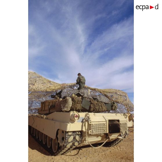 En ZDO (zone de déploiement opérationnel) Olive, un char de combat Abrams-M1 américain entre sous un filet de camouflage tendu dans le désert.
