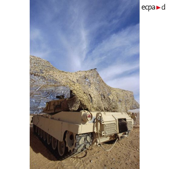 En ZDO (zone de déploiement opérationnel) Olive, un char de combat Abrams-M1 américain entre sous un filet de camouflage tendu dans le désert.