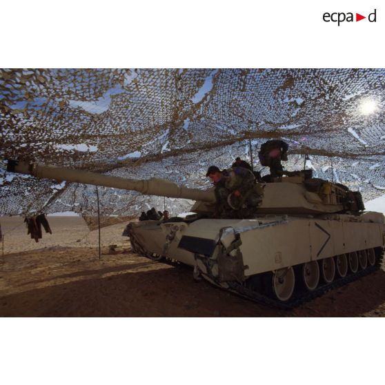 En ZDO (zone de déploiement opérationnel) Olive, un char de combat Abrams-M1 américain entre sous un filet de camouflage tendu dans le désert.