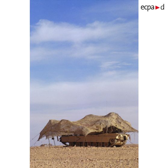 En ZDO (zone de déploiement opérationnel) Olive, un char de combat Abrams-M1 américain est installé sous un filet de camouflage tendu dans le désert.