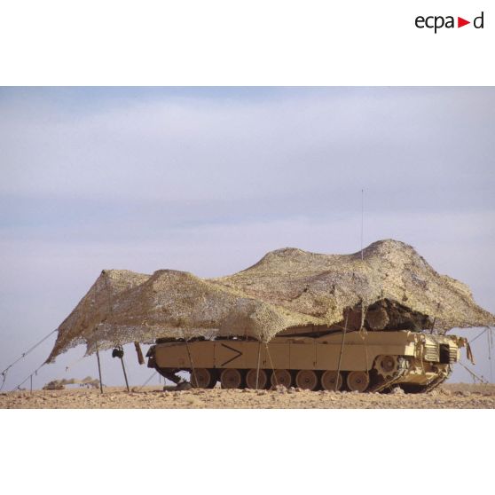 En ZDO (zone de déploiement opérationnel) Olive, un char de combat Abrams-M1 américain est installé sous un filet de camouflage tendu dans le désert.