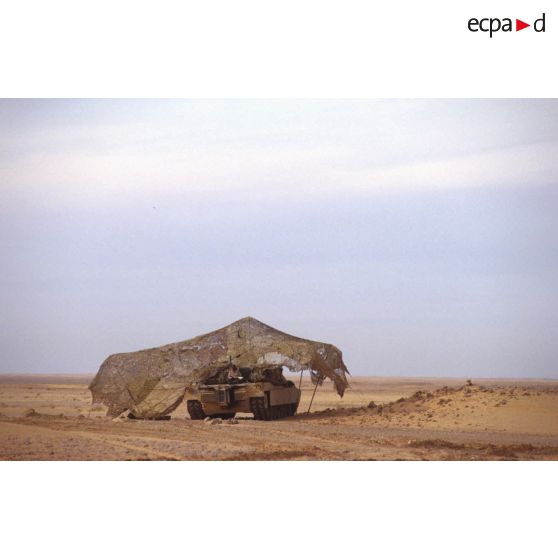 En ZDO (zone de déploiement opérationnel) Olive, un char de combat Abrams-M1 américain est installé sous un filet de camouflage tendu dans le désert.