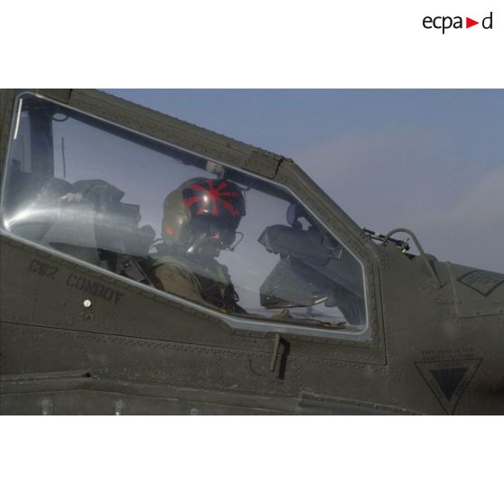 En ZDO (zone de déploiement opérationnel) Olive, portrait d'un copilote-tireur d'hélicoptère de combat américain Hughes-AH 64 Apache au cockpit, verrière latérale relevée.
