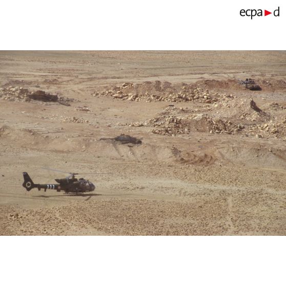 Un hélicoptère de combat Gazelle posé dans la zone de Rochambeau sur une position irakienne à proximité de chars de combat T-55 et d'un transport de troupes chenillé MT-LB irakiens détruits.