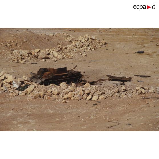 Carcasse de char de combat T-55 irakien calciné dont seul le châssis subsiste dans la zone de Rochambeau. Non loin au sol, une mitrailleuse lourde DShKMT de 12,7 mm.