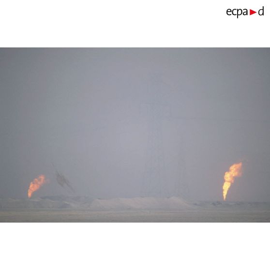 Puits de pétrole en feu derrière un pylone électrique.
