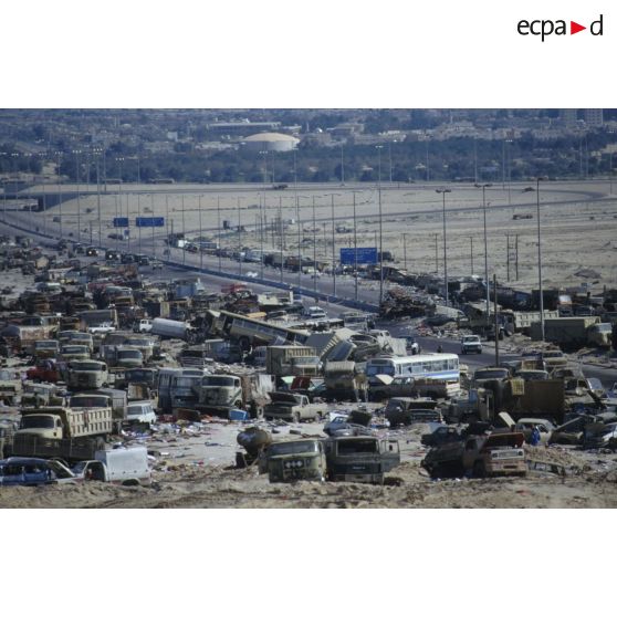 Un convoi de véhicules alliés emprunte la route au milieu d'un cimetière d'épavse de camions et de blindés irakiens détruits ou abandonnés à la sortie de Koweit City.