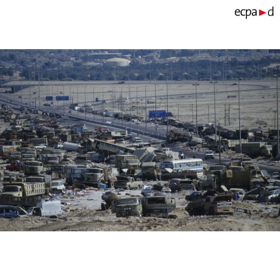 Un convoi de véhicules alliés emprunte la route au milieu d'un cimetière d'épavse de camions et de blindés irakiens détruits ou abandonnés à la sortie de Koweit City.