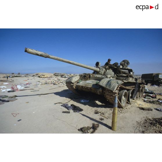 Blindés et camions irakiens détruits ou abandonnés à la sortie de Koweit City : un char de combat T-55 exploré par un militaire allié.