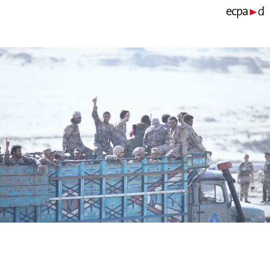 Des soldats saoudiens debout à l'arrière d'un camion civil saluent l'objectif.