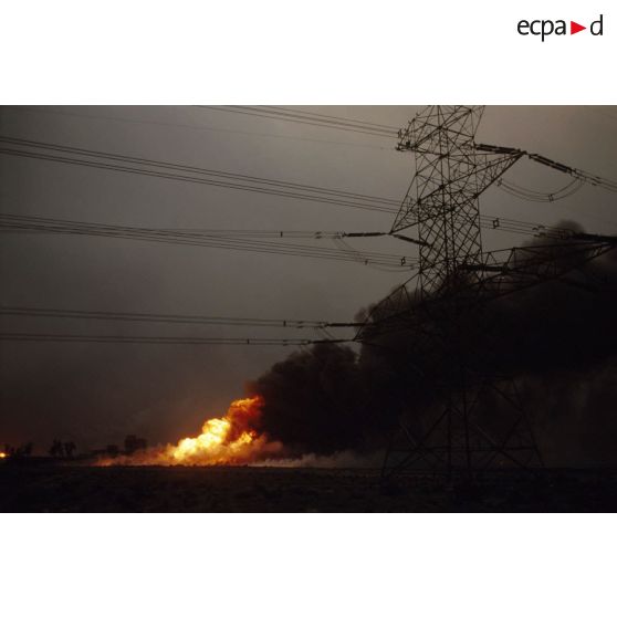 Puits de pétrole en feu aux environs de Koweit city derrière un pylone électrique.