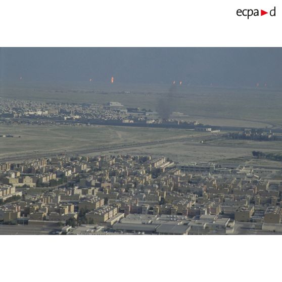 Vue aérienne de la ville de Koweit City. A l'arrière-plan, des puits de pétrole brûlent.