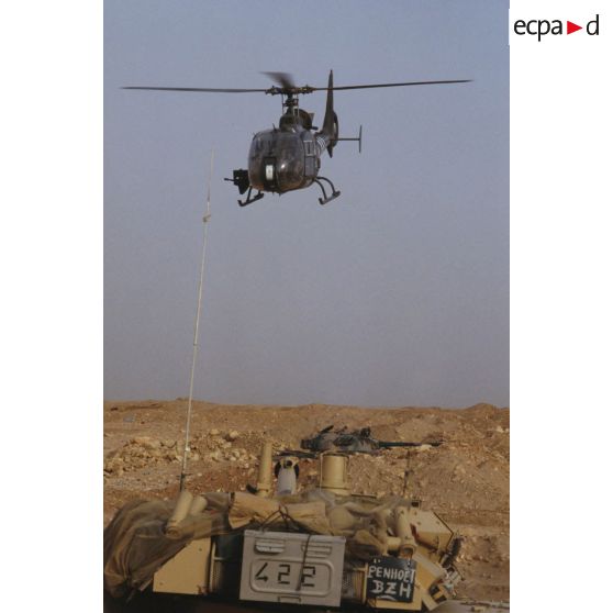 Un hélicoptère de combat Gazelle Canon vole vers l'objectif avec au premier plan un blindé de reconnaissance AMX-10 RC. Au second plan une tourelle de char de combat T-55 irakien.