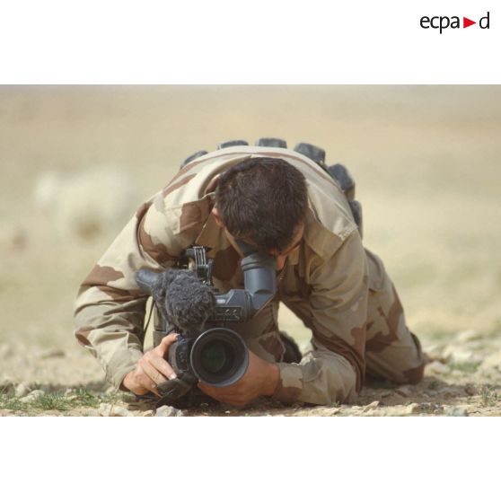 Un brigadier caméraman de l'ECPA (Etablissement cinématographique et photographique des Armées) filme à terre en direction de l'objectif.