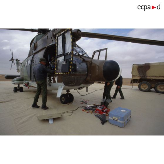 Des mécaniciens de l'ALAT (aviation légère de l'armée de terre) s'affairent autour d'un hélicoptère de transport Puma Orchidée (observatoire radar cohérent héliporté d'investigation des éléments ennemis) au sol.