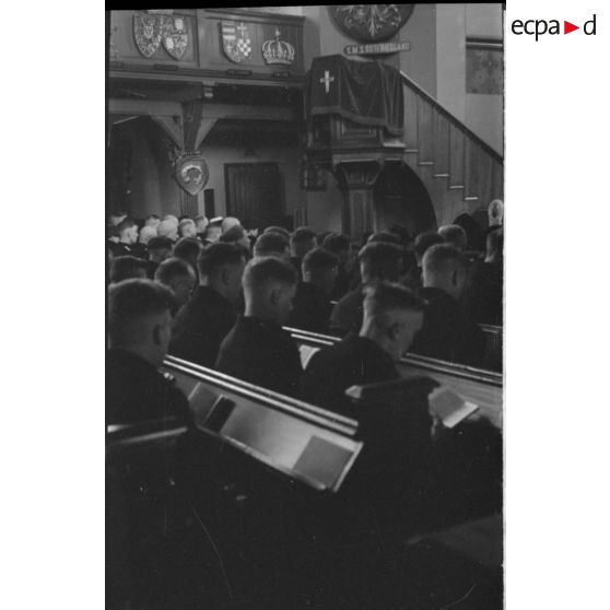 Le prêtre va s'exprimer du haut de la chaire et dos à l'emblème du navire allemand SMS Ostfriesland coulé en 1921 aux Etats-Unis.