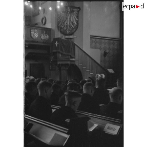 Le prêtre va s'exprimer du haut de la chaire et dos à l'emblème du navire allemand SMS Ostfriesland coulé en 1921 aux Etats-Unis.