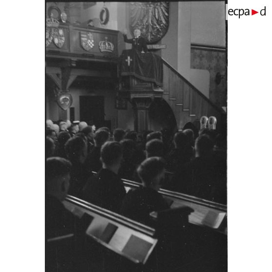 Le prêtre s'exprime devant l'insigne du navire allemand SMS Ostfriesland coulé en 1921 aux Etats-Unis.