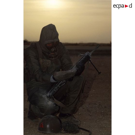 Un soldat du 1er RI en tenue S-3P (survêtement de protection à port permanent) et portant l'ANP (appareil normal de protection) nettoie son fusil d'assaut FAMAS à l'aide d'un gant de décontamination chimique d'urgence lors de l'exercice NBC.