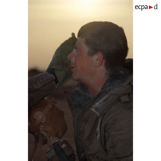 Un soldat en tenue S-3P (survêtement de protection à port permanent) et tenant l'ANP (appareil normal de protection) se fait nettoyer le visage à l'aide d'un gant de décontamination chimique d'urgence par son camarade lors de l'exercice NBC du 1er RI.