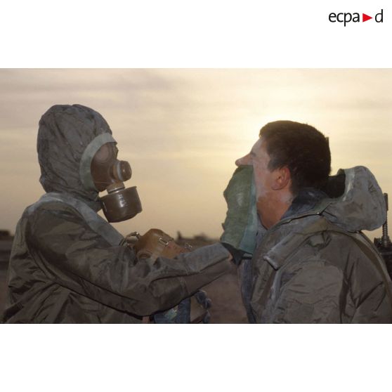 Un soldat en tenue S-3P (survêtement de protection à port permanent) et portant l'ANP (appareil normal de protection) nettoie le visage de son camarade à l'aide d'un gant de décontamination chimique d'urgence lors de l'exercice NBC du 1er RI.