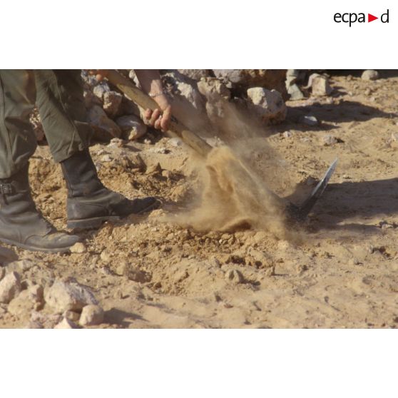 Installation du bivouac du 1er RI pour la nuit, un militaire creuse un trou de combat à la pioche.