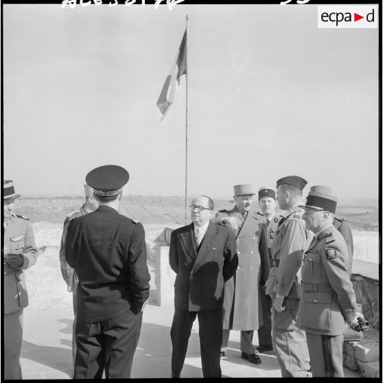 Pierre Métayer, secrétaire d’État aux forces de l'armée de terre, en discussion avec des officiers devant le drapeau tricolore.