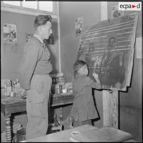 Un petit garçon écrit au tableau sous le regard de l’instituteur dans une école de Djezia.
