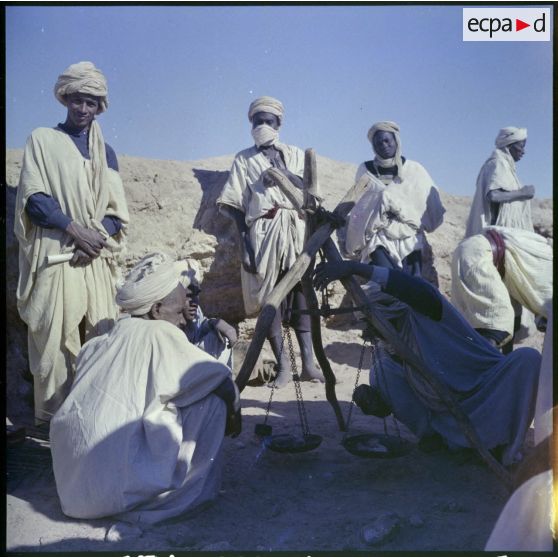 Un groupe d'hommes autour d'une balance, l'un d'eux pèse des objets.