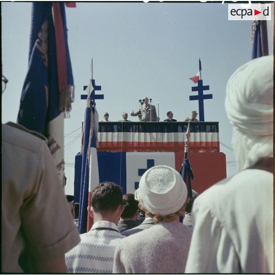 Le général De Gaulle s'adresse à la foule du haut d'un podium orné de croix de Lorraine.