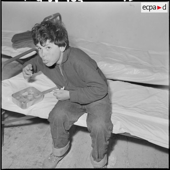 Portrait d'un enfant du foyer de jeunesse de la rue Bab-El-Oued à Alger, en train de manger.