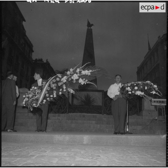 Des hommes tiennent des gerbes de fleurs devant le monument aux morts.