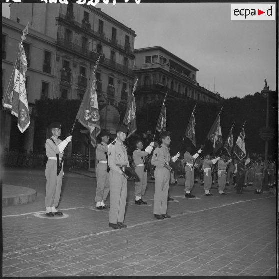 Porte-drapeaux devant le monument aux morts et deux soldats présentant chacun un coussin des décorations.