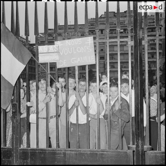 Derrière les grilles du ministère de l'Algérie, de jeunes manifestants brandissent de multiples pancartes.