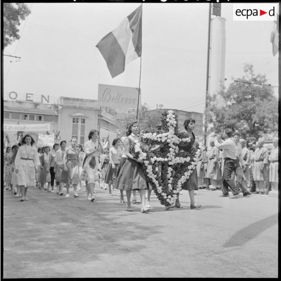 Des femmes venant de Bellevue défilent avec une gerbe de fleurs en forme de croix de Lorraine dans les rues de Constantine.