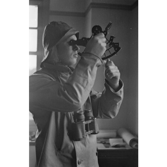 Portrait d'un sous-marinier portant un ciré, coiffé d'une capuche équipé d'une paire de jumelles et d'un sextant.