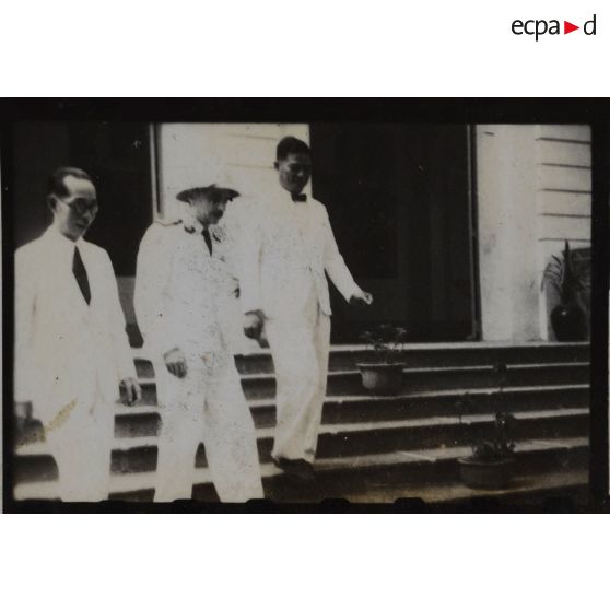 Trois personnalités, dont le président Hoach, descendent les marches d'un bâtiment. [description provisoire]