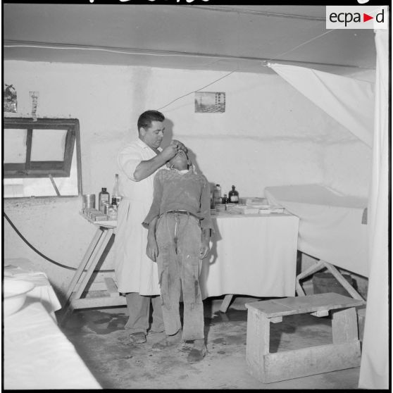 Centre de regroupement de Sahel. Infirmerie. Un infirmier de 1ère classe soigne un enfant atteint d'affections occulaires.