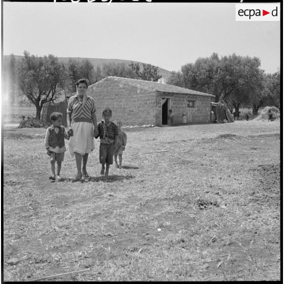 Centre de regroupement d'Ouled Ali. Une femme et ses enfants devant une maison.