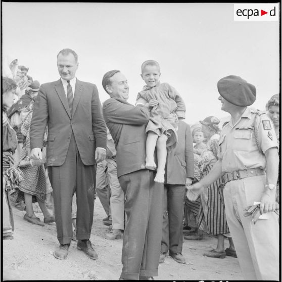 Le Premier ministre Michel Debré accompagné de Mr Delouvrier, délégué général, prend dans ses bras un enfant du village de Tikichourt, venu l'acclamer.