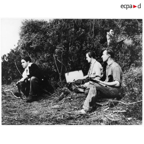 Un opérateur radio transmet un message sur un poste émetteur-récepteur (valise radio), sous la protection de résistants corses équipés de pistolets-mitrailleurs Sten Mk II.