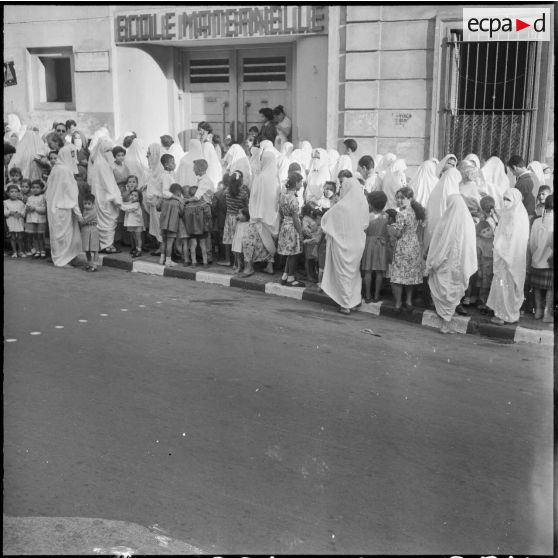Rassemblement des élèves accompagnés par leurs parents devant l'entrée de l'école maternelle.