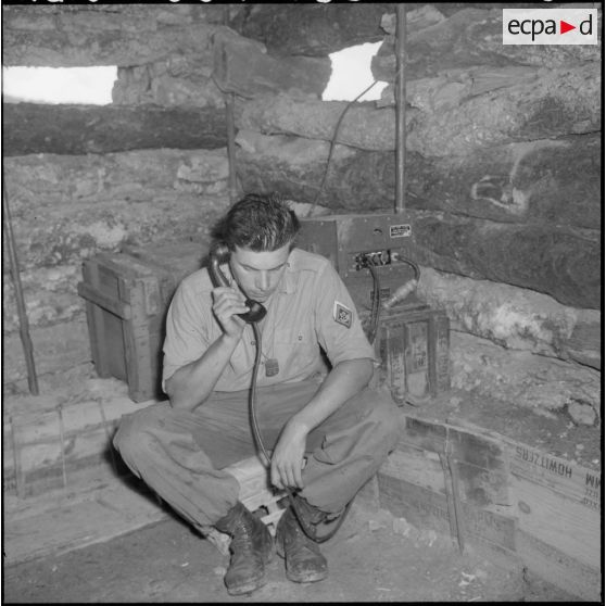 Portrait du sergent Thiebaut François (57 2/A), originaire de Essey-lès-Nancy (Meurthe-et-Moselle) et conducteur-margeur dans le civil, au téléphone à l'intérieur d'un abri fortifié.