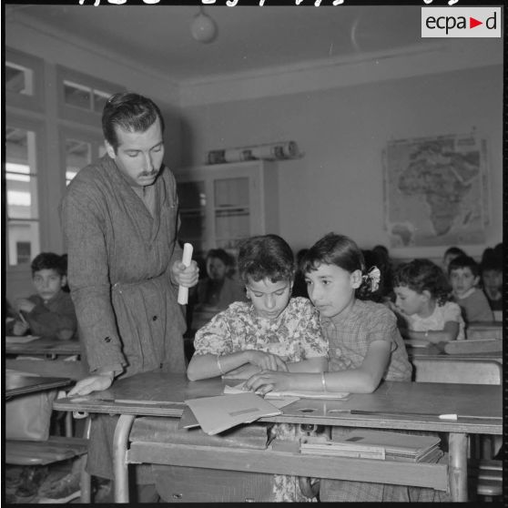 A l'intérieur d'une salle de classe, l'instituteur Vayssier, originaire de Toulouse, supervise le travail de deux élèves.