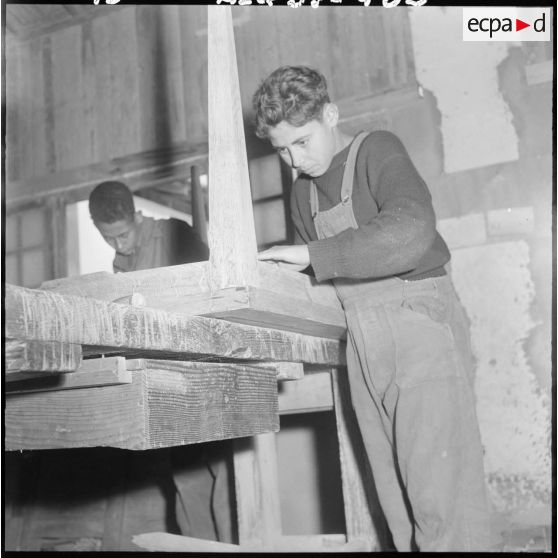 Centre de formation de la jeunesse algérienne : à l'intérieur de l'atelier de menuiserie, portrait d'un élève âgé de 18 ans, de Dupleix, en plein travail.