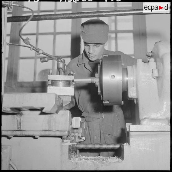 Centre de formation de la jeunesse algérienne : à l'intérieur de l'atelier de mécanique, portrait d'un élève âgé de 17 ans, de Cherchell, attentif au tournage d'une pièce.
